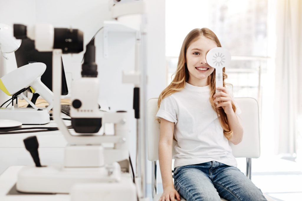 Girl covering one of her eyes and reading signs from the table while having her eyesight tested